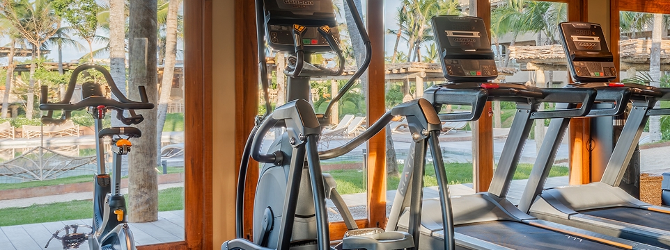 Academia com esteiras e bicicleta, com vista para o jardim e coqueiros.